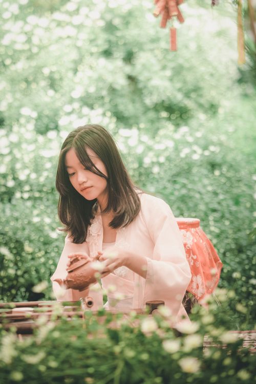 Free Asian woman enjoying a peaceful tea ceremony in a vibrant garden, surrounded by greenery and flowers. Stock Photo