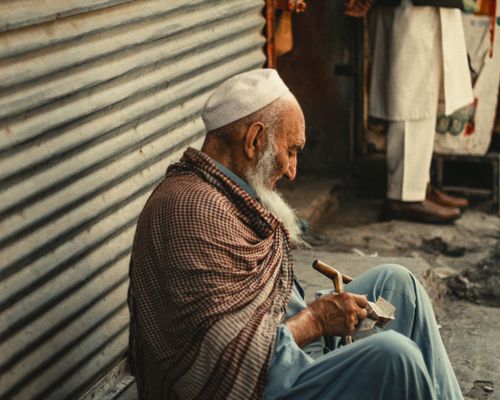Free A senior man crafting wooden items in a bustling Peshawar market, highlighting local life. Stock Photo