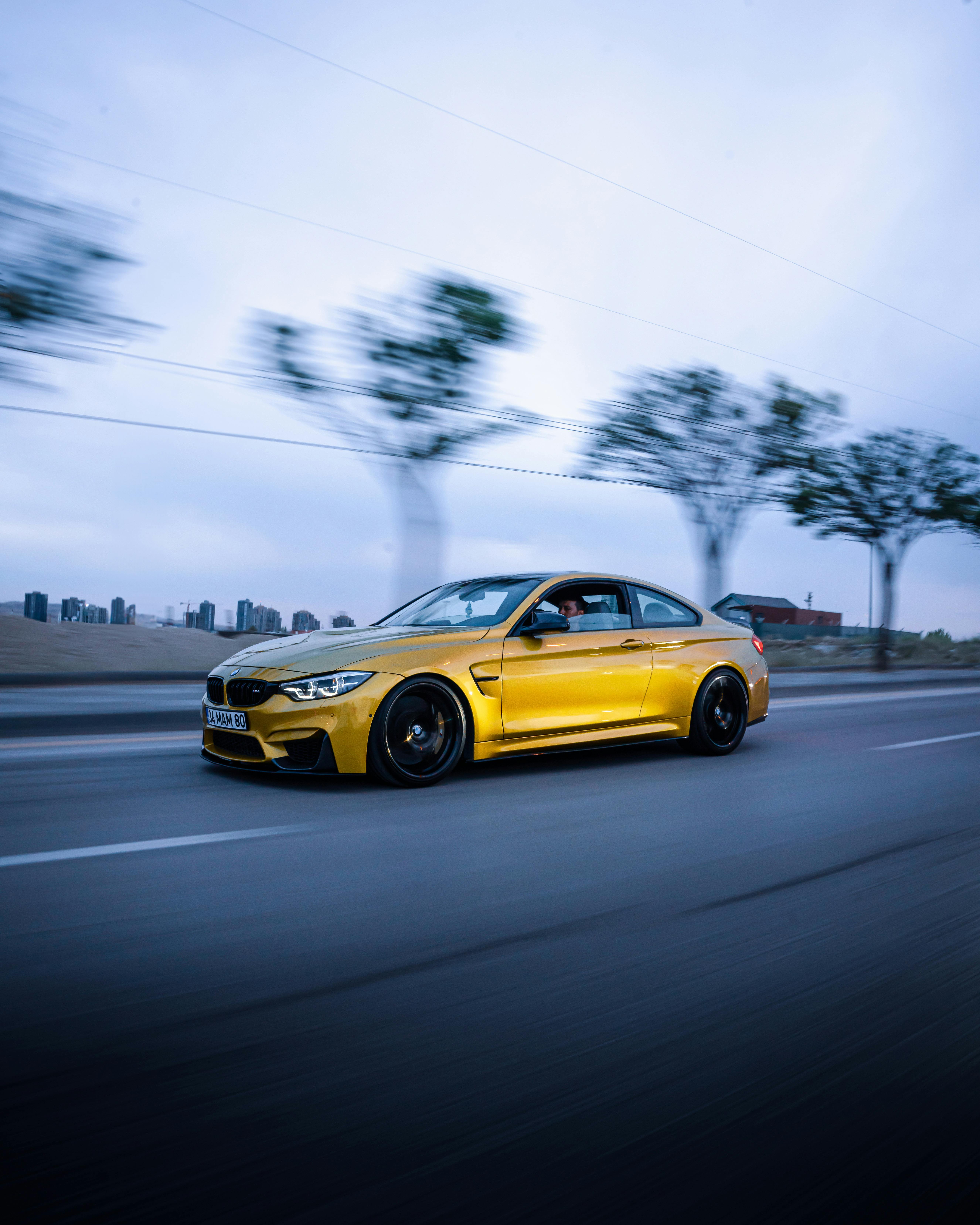 A sleek yellow sports car speeds along a highway in Ankara, Türkiye, captured in motion with blurred trees.