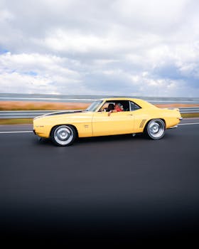 A classic yellow car speeds along a highway in Ankara, Türkiye, under a cloudy sky.
