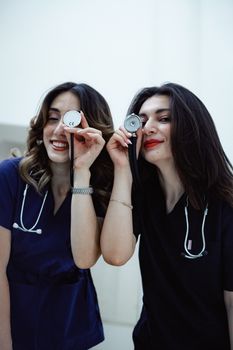 Two female doctors with stethoscopes playfully posing indoors in Baku, Azerbaijan.