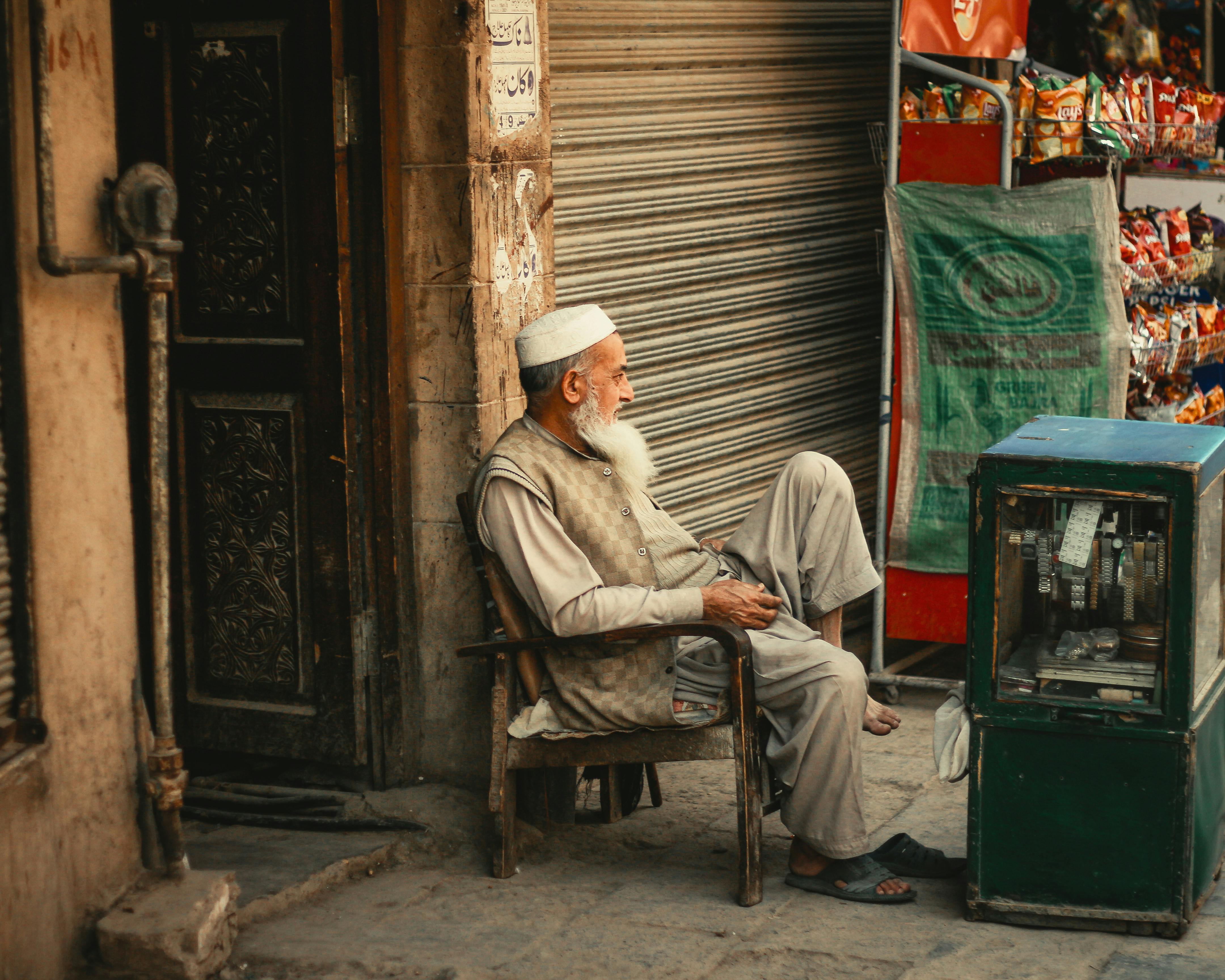 Elderly man seated by a shop in Peshawar, capturing local culture and street life.