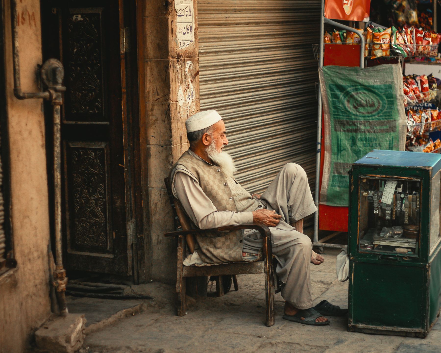 Elderly man seated by a shop in Peshawar, capturing local culture and street life.