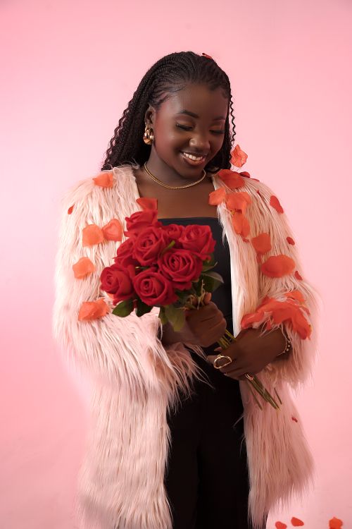 Free Smiling woman in faux fur coat holding red roses against a pink backdrop. Perfect for Valentine's themes. Stock Photo