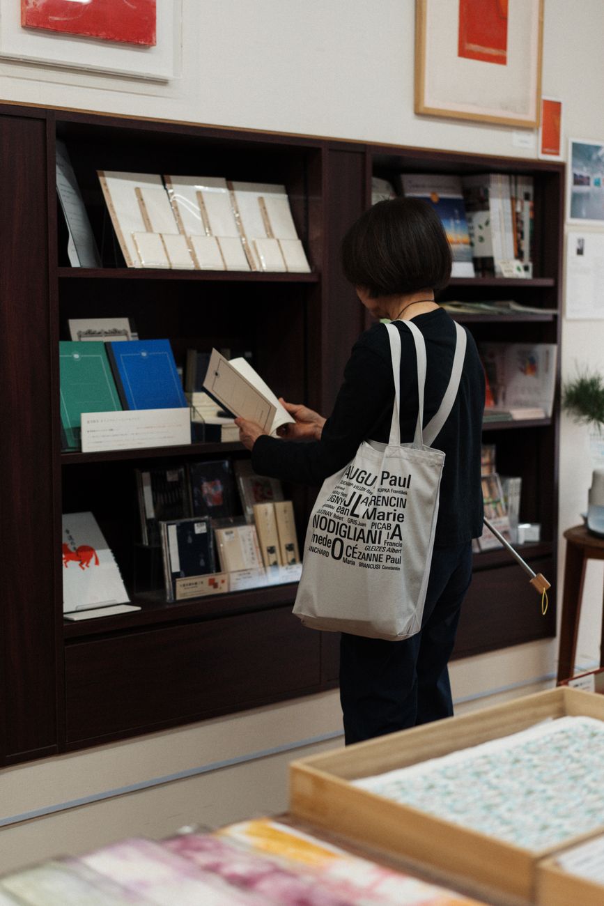 Woman browsing books in a Kyoto shop, carrying a literary-themed tote