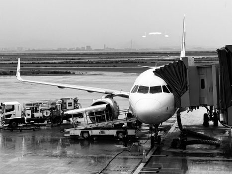 Black and white photo of a passenger plane at a rainy airport gate.
