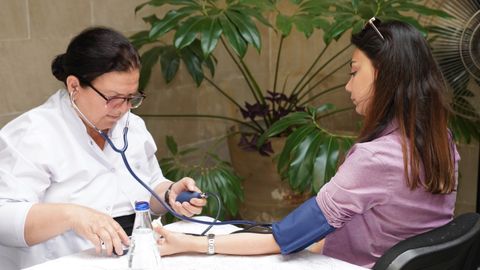 A healthcare worker measures a woman's blood pressure in an outdoor setting, emphasizing wellness and care.