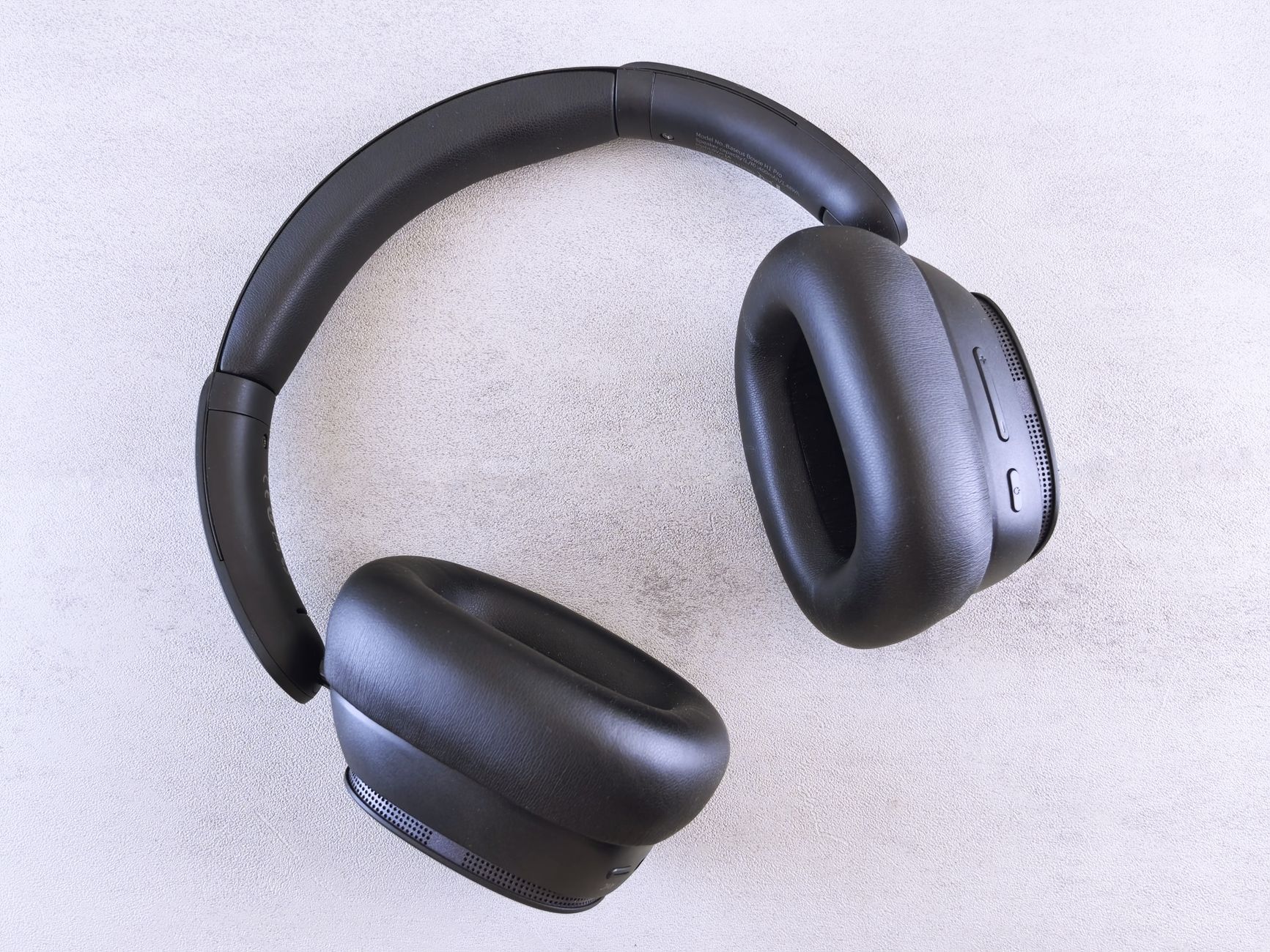 Top view of modern black over-ear wireless headphones on a light textured surface.