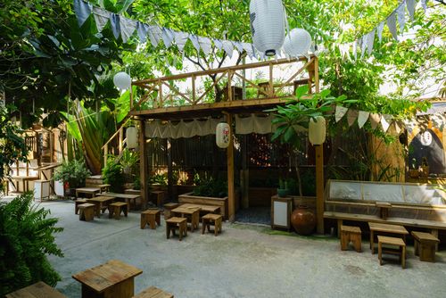 Free Outdoor cafe patio with wooden seating surrounded by lush greenery and lanterns. Stock Photo