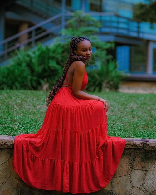 Free Smiling young woman in a vibrant red dress sitting outdoors on a stone wall. Stock Photo