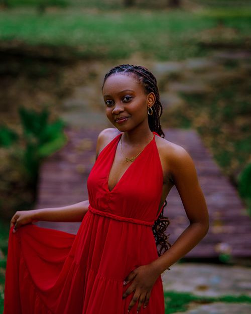 Free A stylish young woman poses confidently in a vibrant red dress in an outdoor setting. Stock Photo