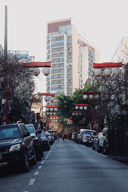 Free Charming city street with red lanterns, framed by modern architecture and parked cars, daytime. Stock Photo