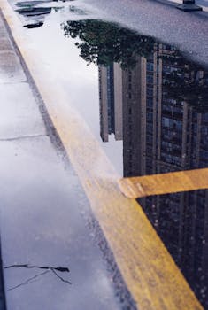 Urban skyscraper reflected in a rain puddle on the street, with a mood of tranquility and urban life.