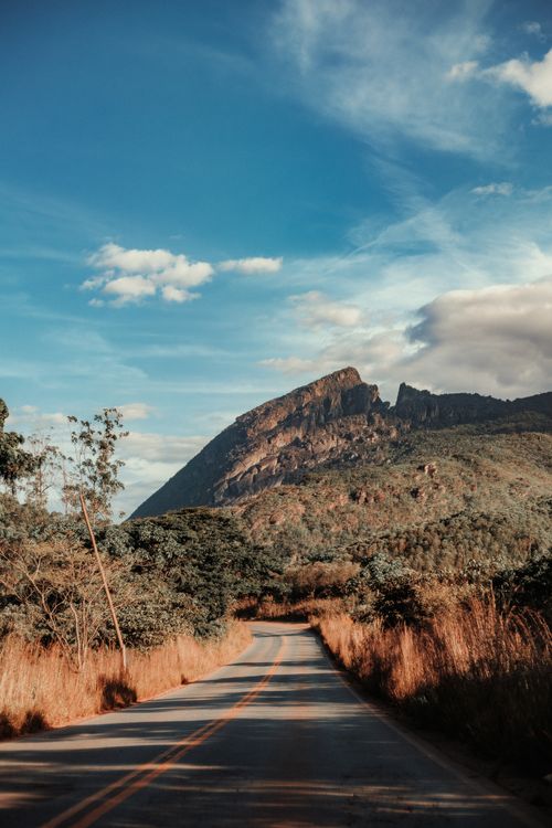 Free A picturesque road leading to a mountain under a bright blue sky, capturing the essence of rural tranquility. Stock Photo