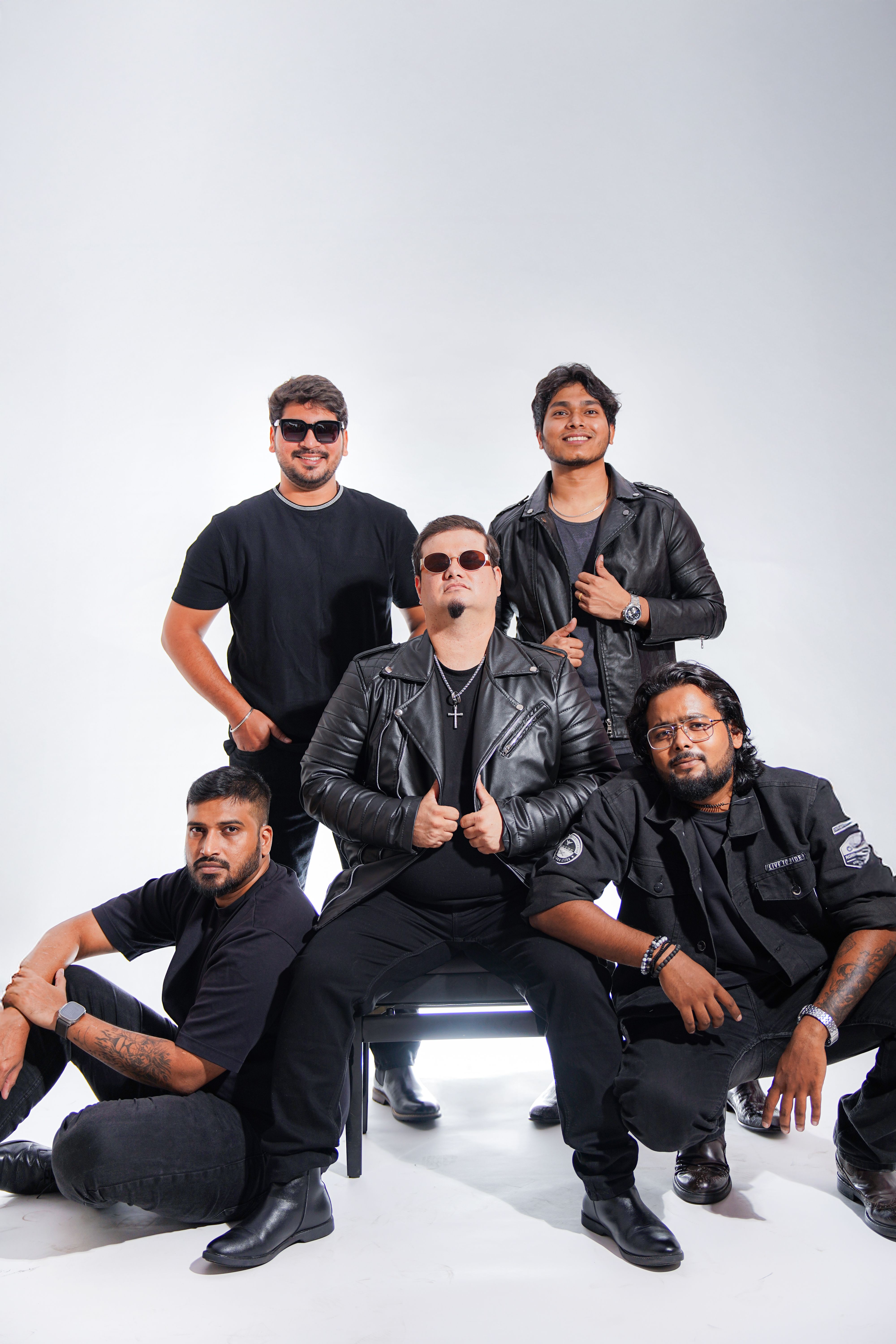 A group of five men wearing black outfits poses confidently in a studio setting.