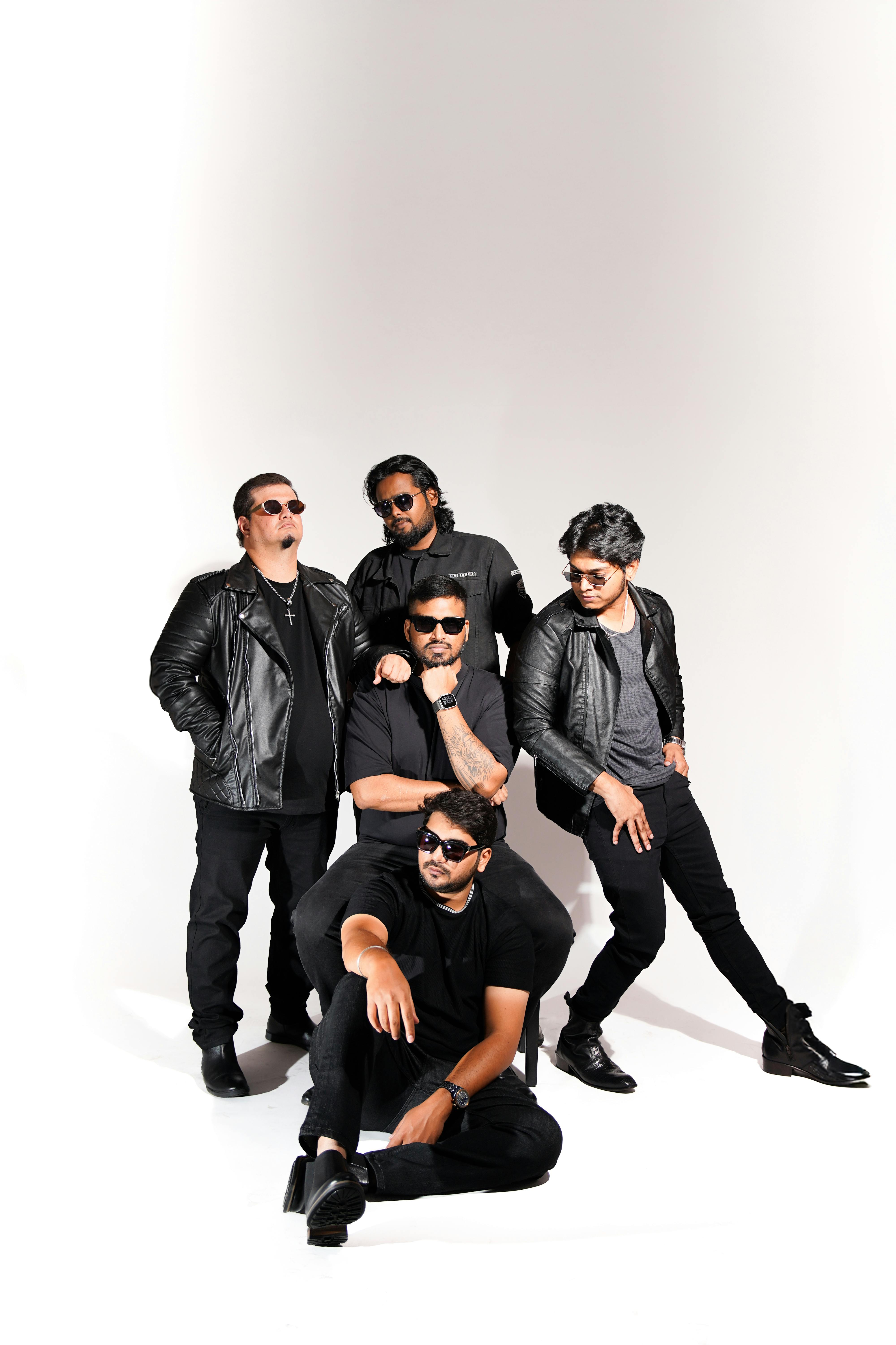 Five men dressed in black outfits, posing confidently in a studio setting.
