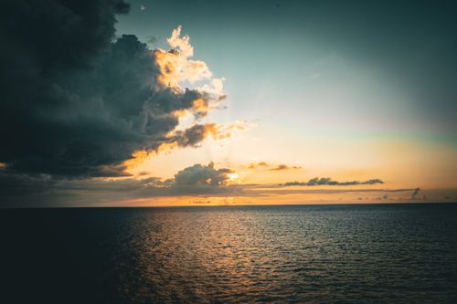 Free Stunning sunset with dramatic clouds over an expansive ocean, captured at dusk. Stock Photo