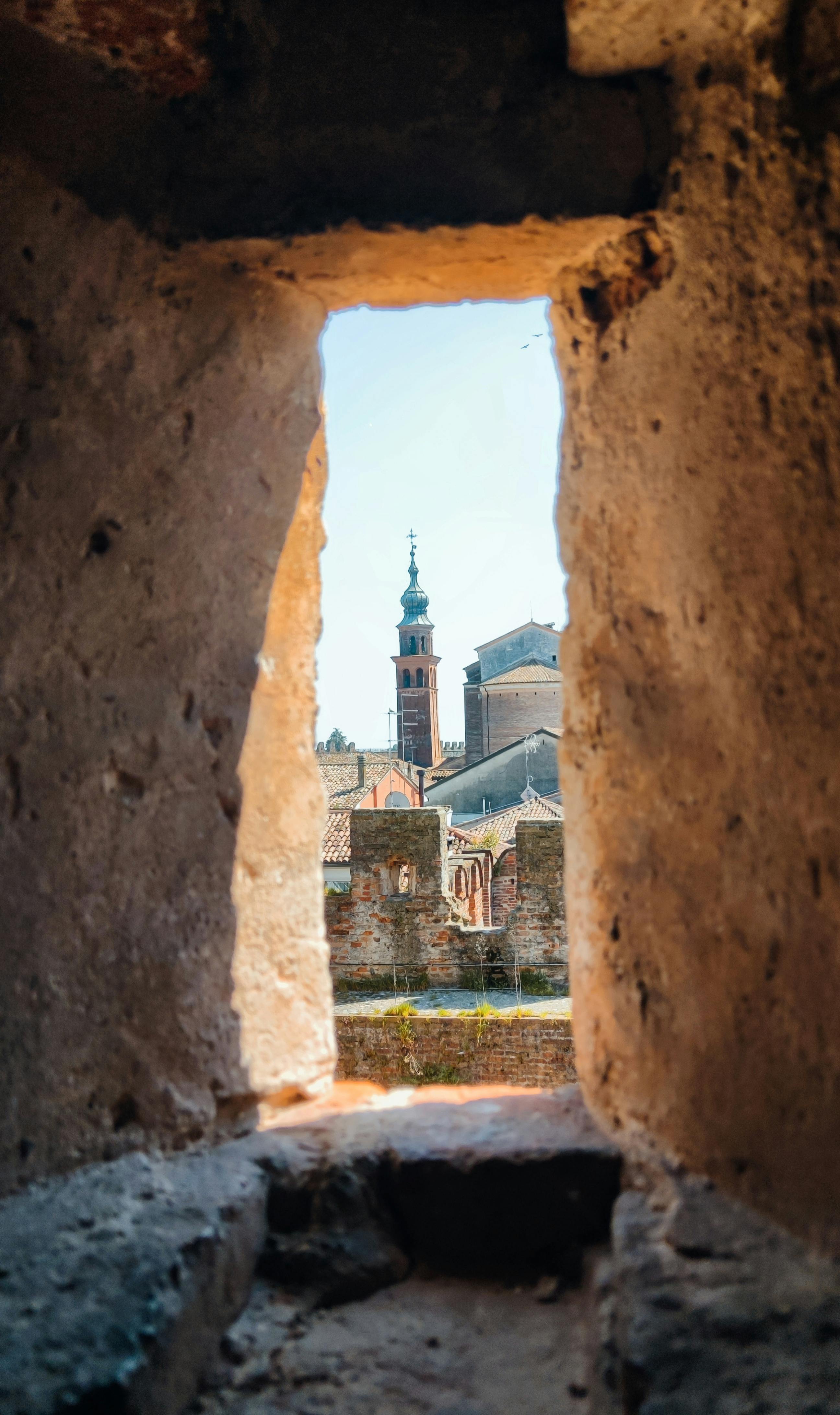Gratis Attraverso un antico arco in pietra si possono ammirare una torre storica e alcuni edifici, sottolineando così la fusione di elementi architettonici. Foto a disposizione