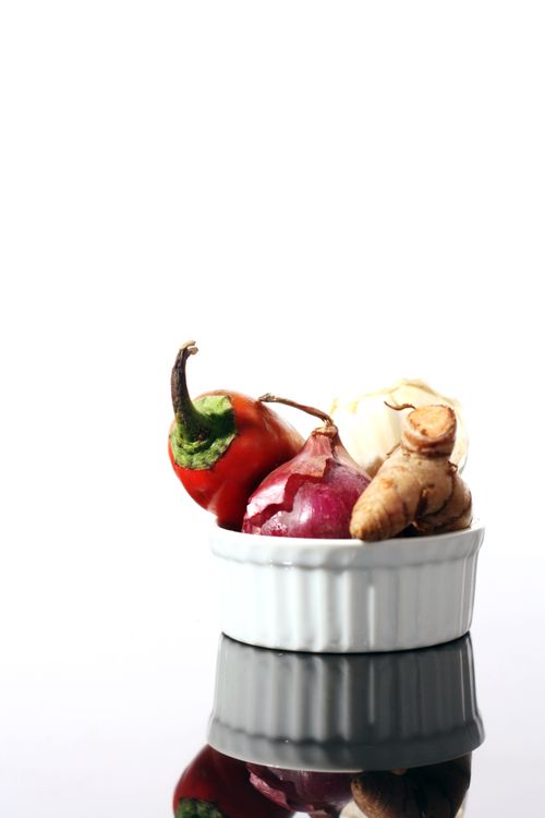 Free Vibrant vegetables including onion, ginger, and pepper in a ceramic bowl on a reflective surface. Stock Photo