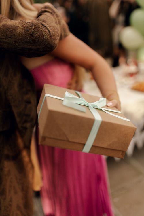 Free A woman in a pink dress receives a gift wrapped in brown paper with a teal ribbon at an outdoor event. Stock Photo