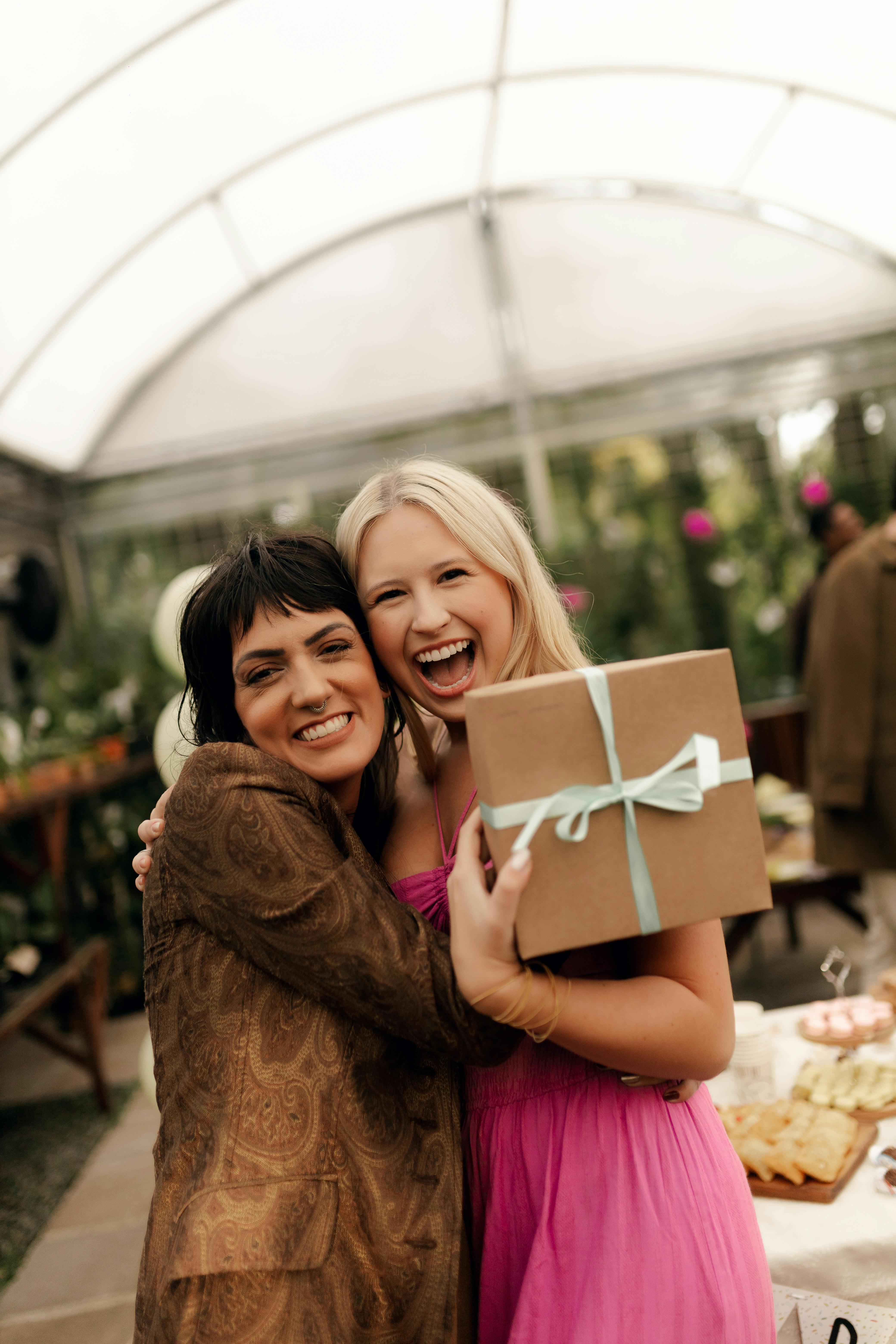 Gratis Due amiche si scambiano con gioia un regalo a una festa, immortalando un momento di felicità in casa. Foto a disposizione