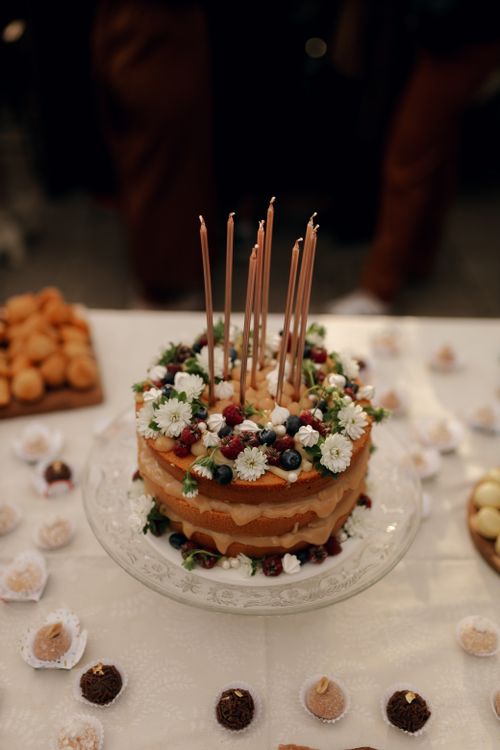 Free A rustic cake adorned with flowers and berries, surrounded by assorted sweets on a decorated table. Stock Photo