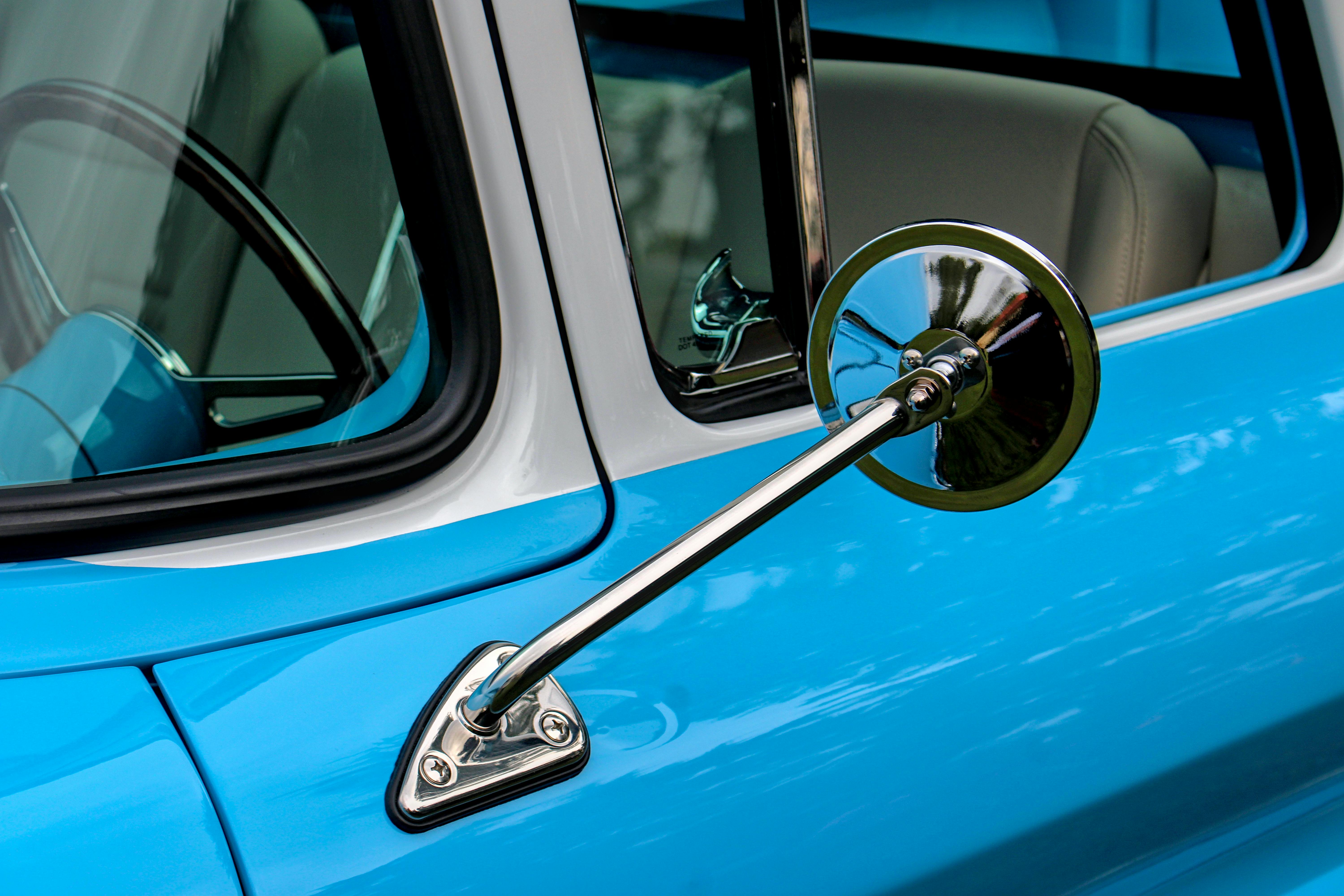 Detailed view of a classic car's chrome side mirror and window trim with vibrant blue paint.