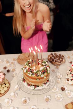 A woman celebrates her birthday with a decorated cake surrounded by desserts.