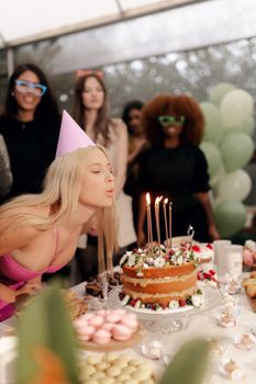 A woman blows out candles on a birthday cake surrounded by friends at a party.