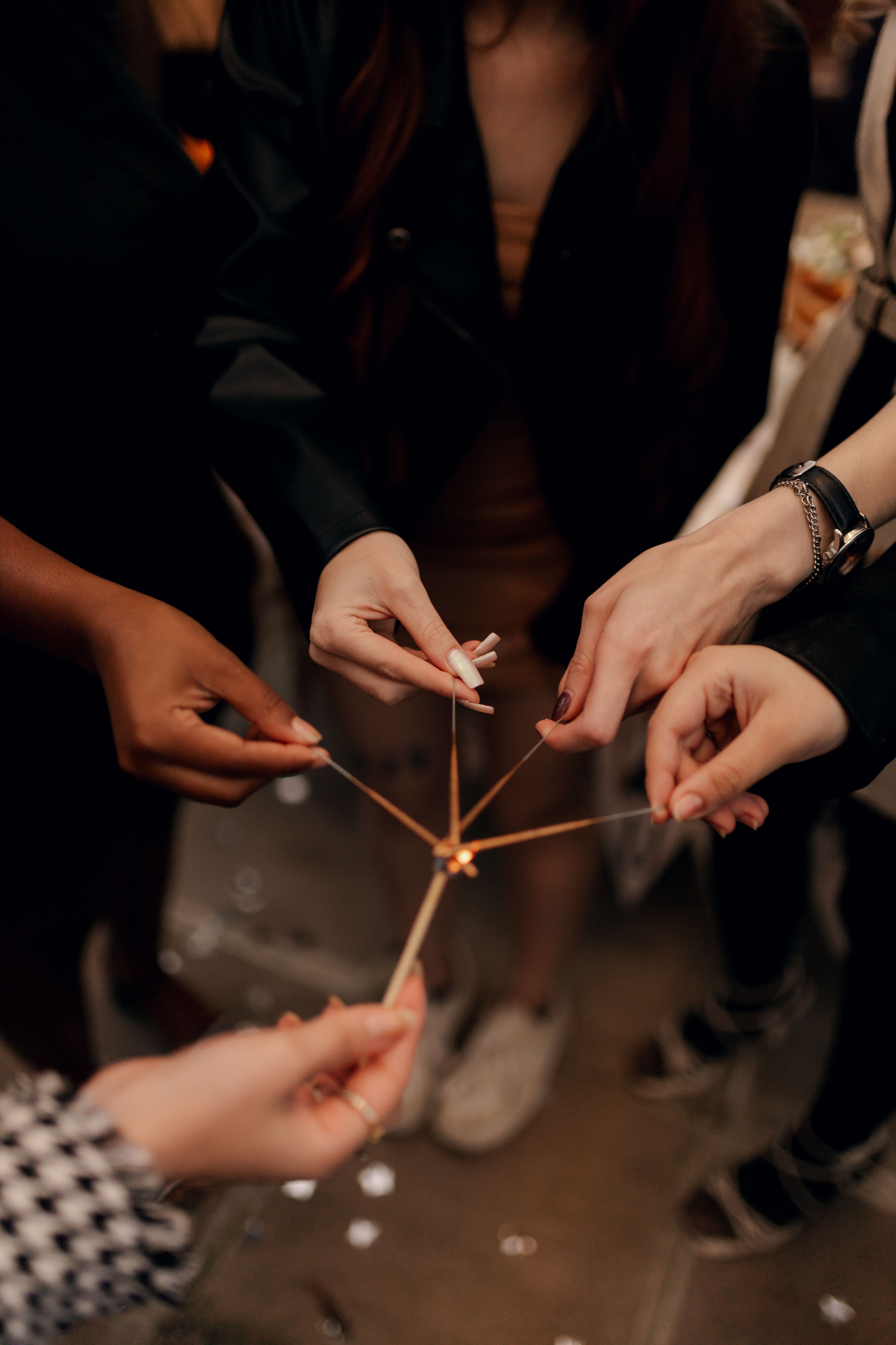 Close-up of diverse hands lighting sparklers during a festive indoor gathering, symbolizing unity and celebration.