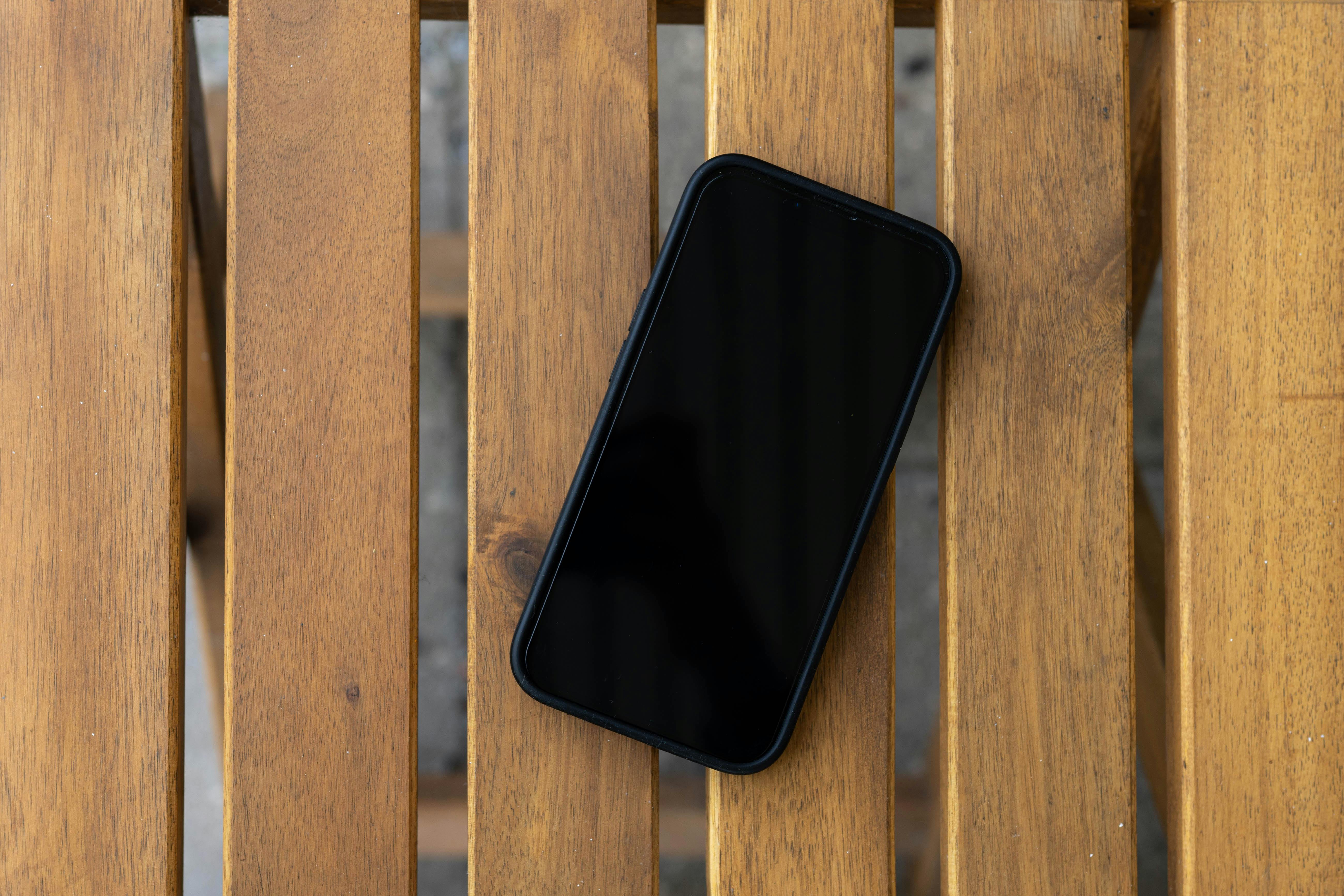 bezplatná Chytrý telefon s černou obrazovkou leží na dřevěném roštovém stole, pohled shora. Základová fotografie