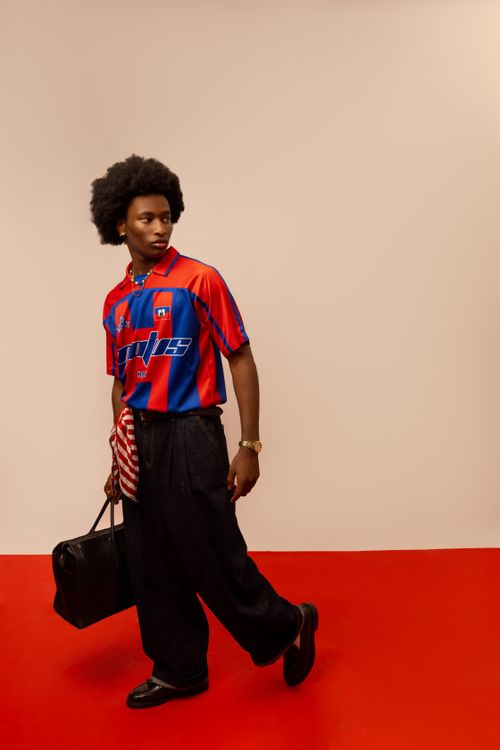 Free Fashion-forward young adult in red and blue retro jersey holding a bag indoors, on a red floor. Stock Photo