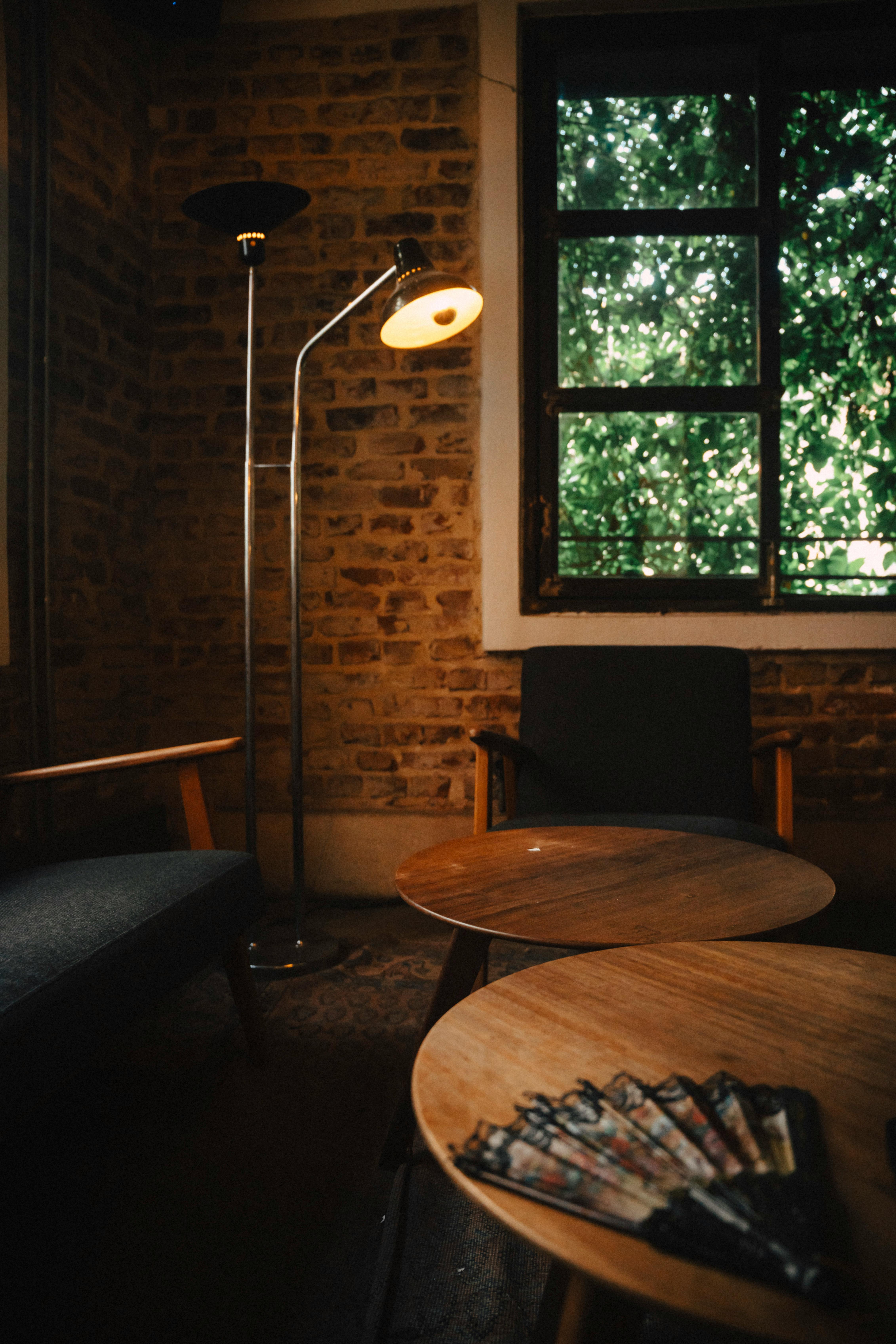 Free Warm cafe interior with wooden tables, lamp, and brick walls beside a window view. Stock Photo
