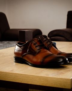 Stylish brown leather shoes placed on a wooden table in a cozy indoor setting.