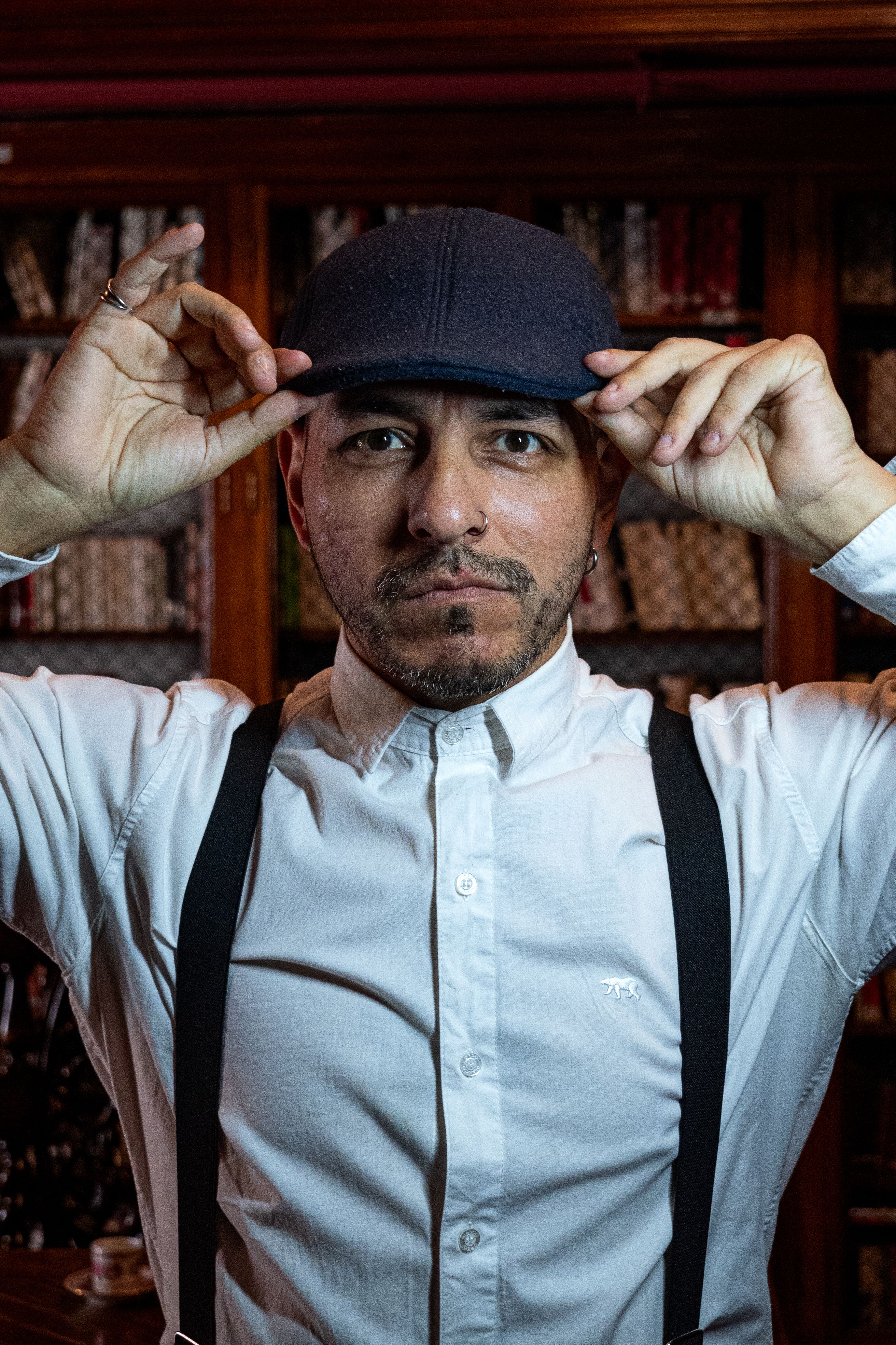 Stylish man in white shirt and cap posing confidently in a classic Buenos Aires library.
