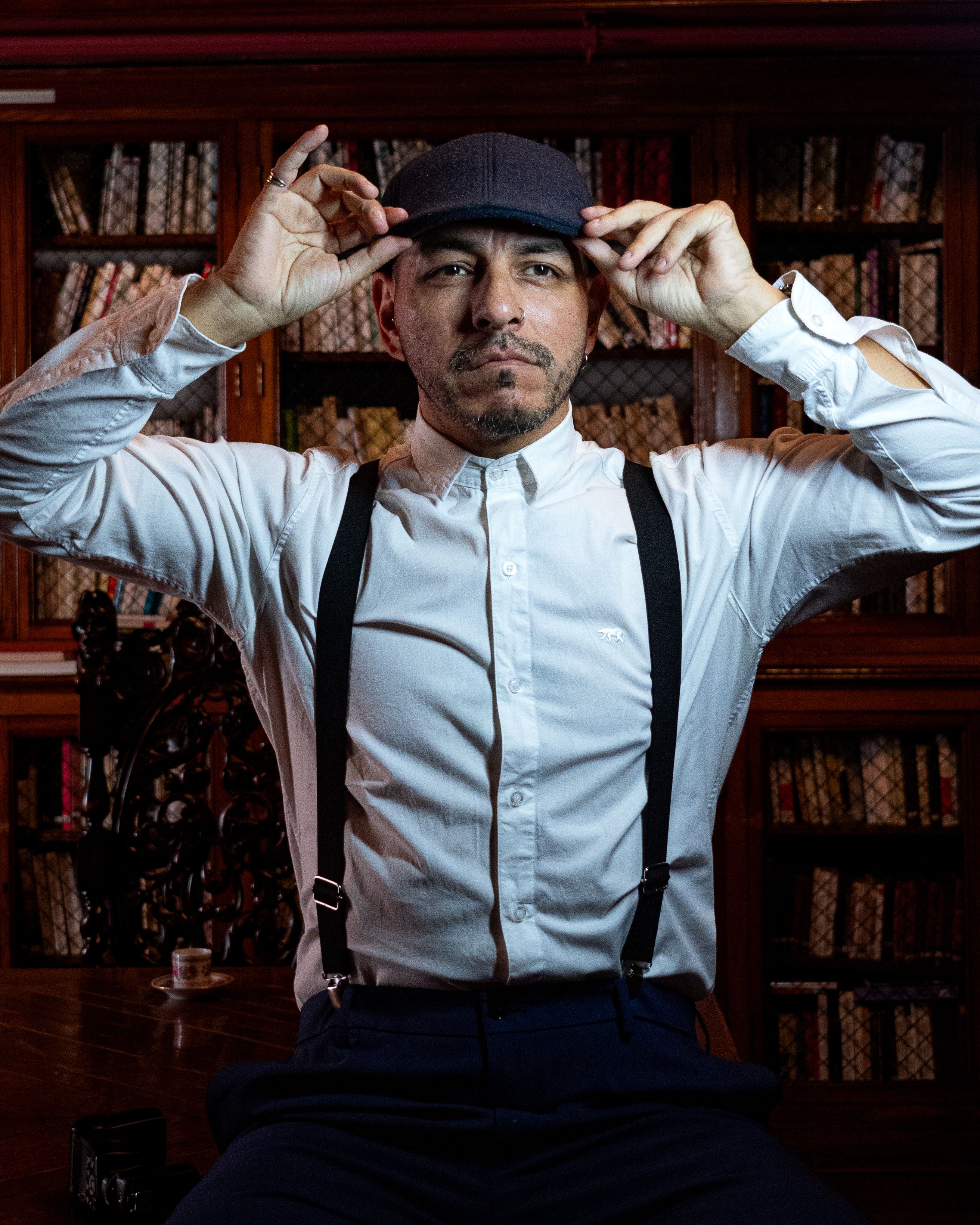 A man in vintage attire adjusts his cap, set in a classic Buenos Aires library.