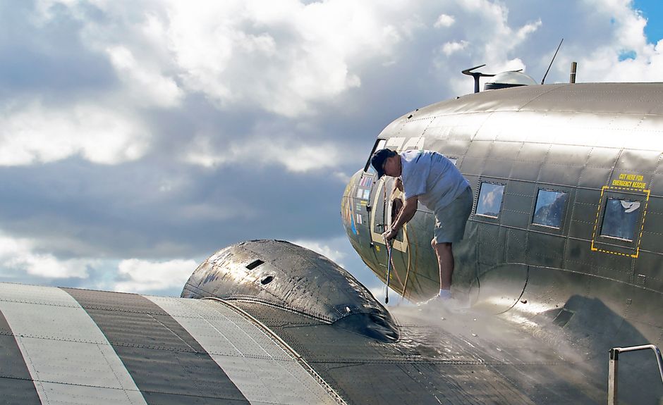 A worker performing maintenance on a C-47 aircraft wing under bright skies in Titusville, Florida. A worker performing maintenance on a C-47 aircraft wing under bright skies in Titusville, Florida.