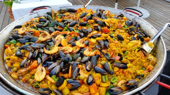 Wide paella pan heaped with black mussels, small shrimp, peas, carrots and peppers in yellow rice