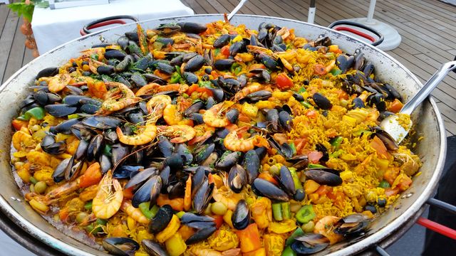 Close-up of a large pan of colorful seafood paella outdoors.