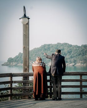 Senior couple on a wooden deck gazing at the ocean, a peaceful moment captured by the sea.