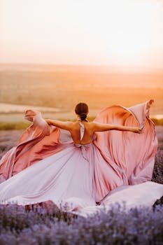 A woman in a flowing dress dances gracefully in a lavender field during a vibrant sunset.