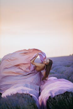 A woman elegantly posed in a flowing lavender dress amidst a serene lavender field at sunset.