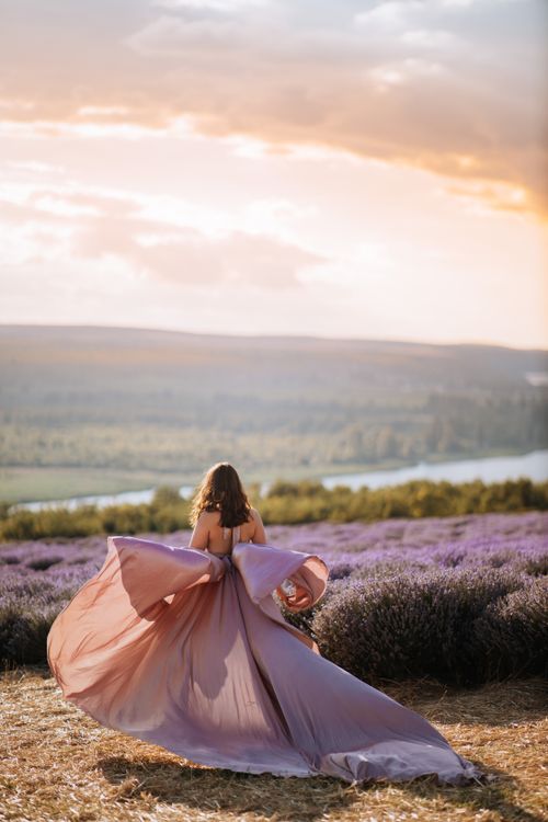 Free A woman in a flowing pink dress enjoying a picturesque lavender field at sunset. Stock Photo