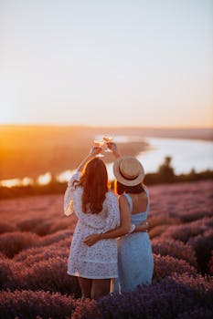 Two women enjoying a sunset in a lavender field, raising glasses in celebration.