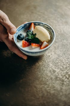 A close-up of a delicious dessert bowl with berries, ice cream, and mint leaves on a textured surface.