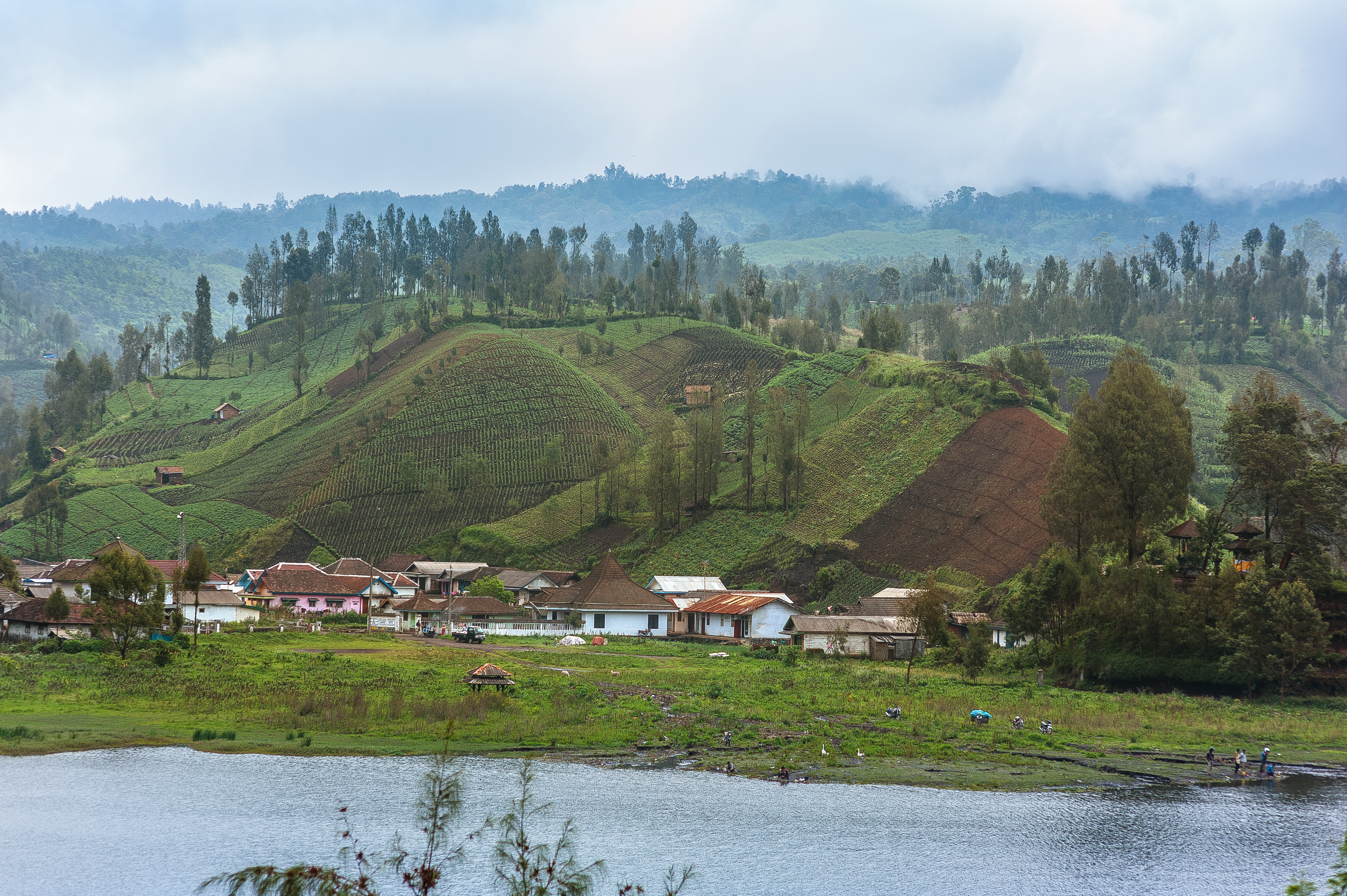 Scenic View Of A Village With Lush, Terraced Hills By A Tranquil Lake.