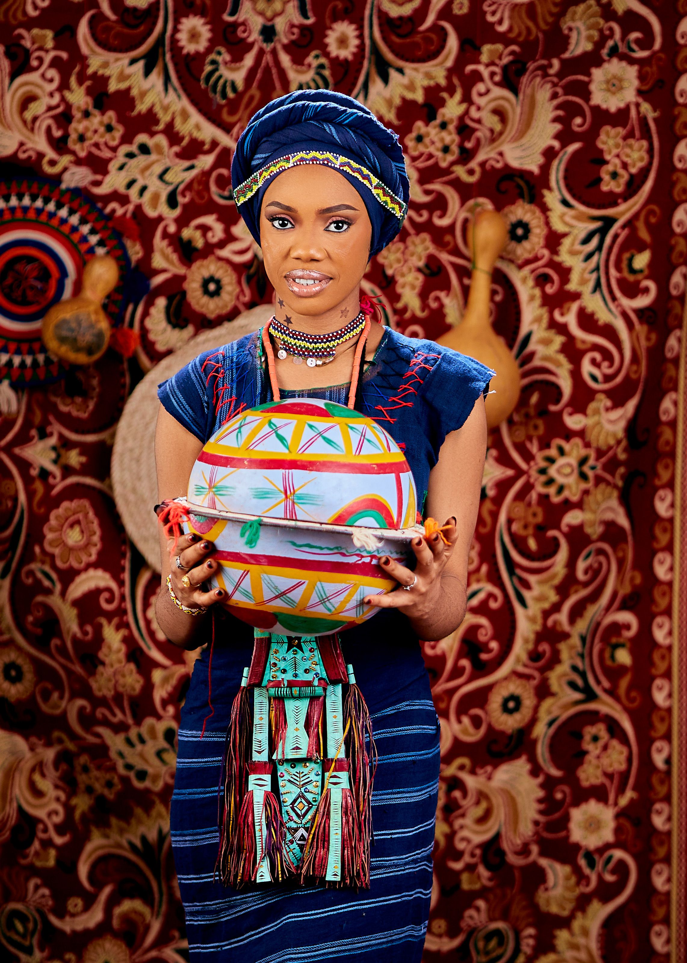 Vibrant portrait of an African woman holding a colorful traditional craft against a patterned background.