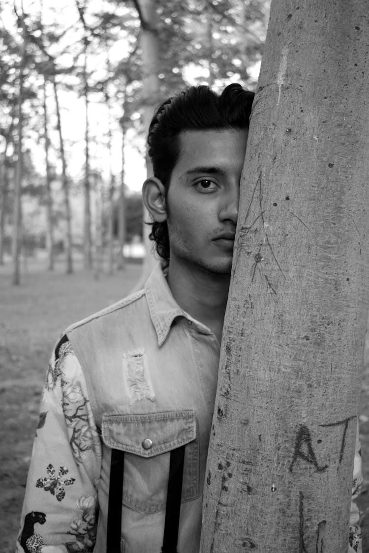 Ethnic Man Hiding Half Of Face Behind Tree Bole