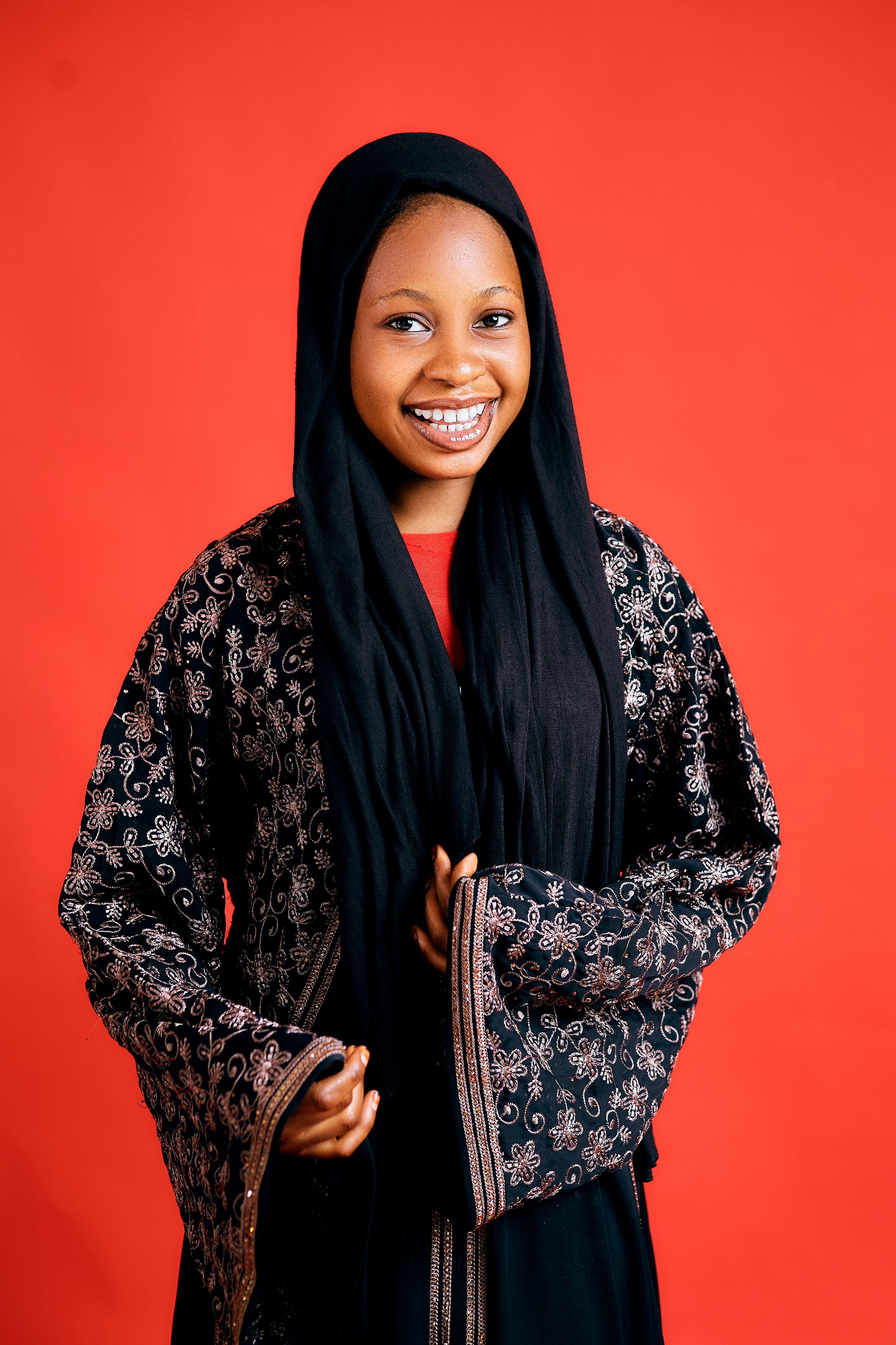 Happy young girl in traditional dress smiling against a vibrant red backdrop.