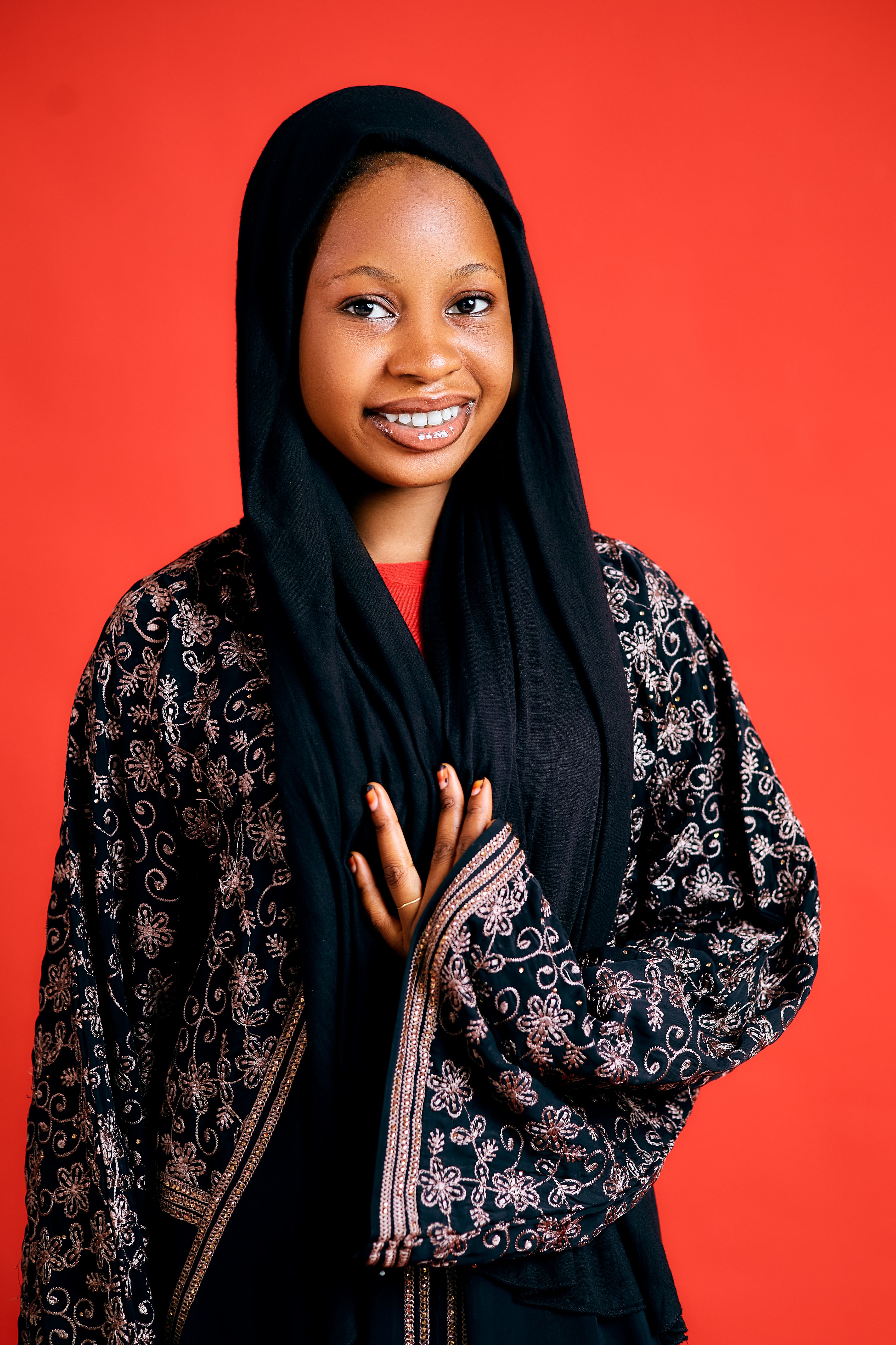 Happy girl in traditional attire with intricate embroidery on vibrant red background.